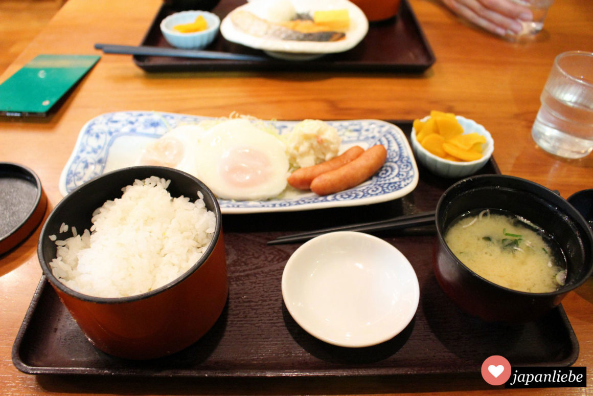 Schnelles, japanisches Frühstück mit Reis, Tsukemono, Eiern, Würstchen und Fisch