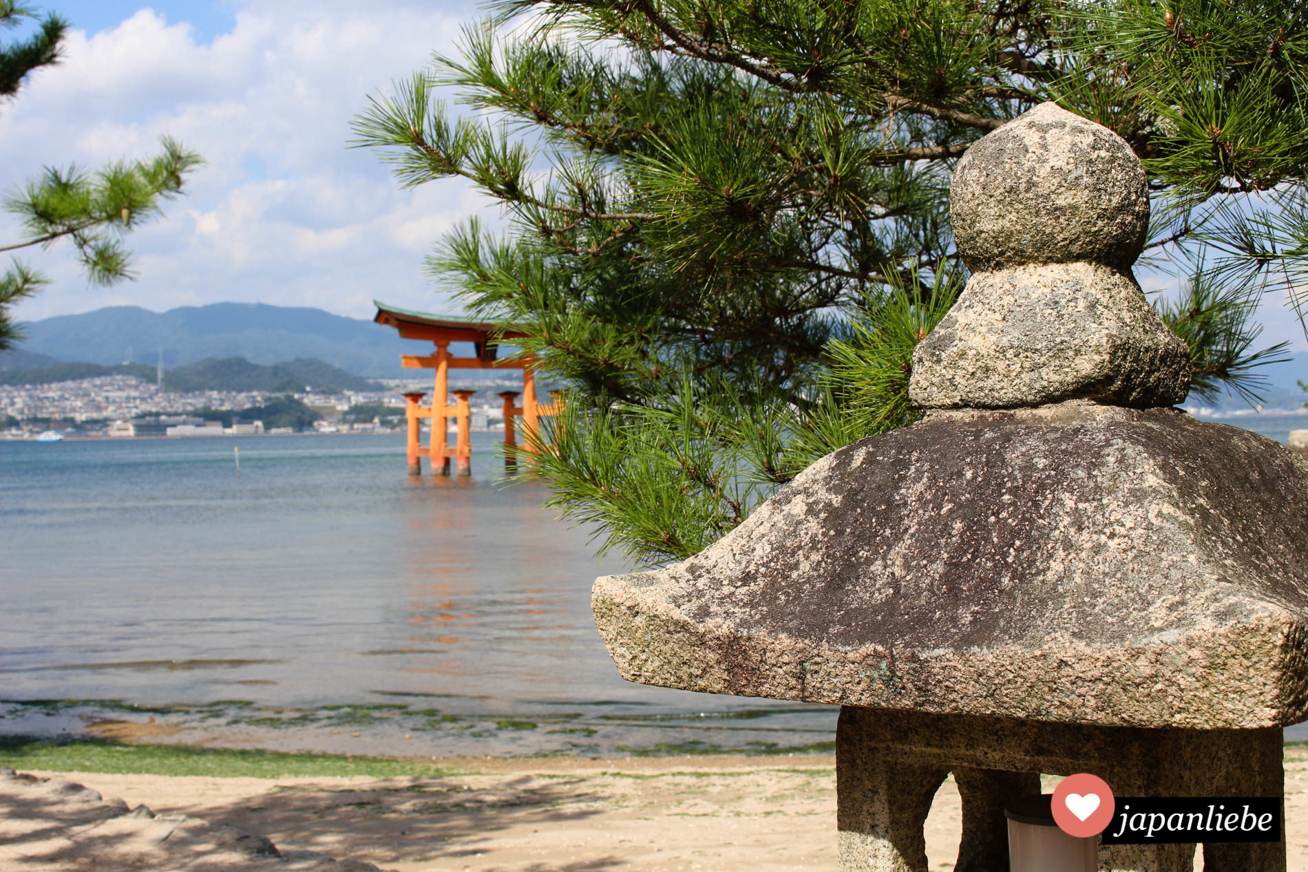 japans berühmtestes torii auf Miyajima vom Strand aus fotografiert, inklusive Steinlaterne im Bild.