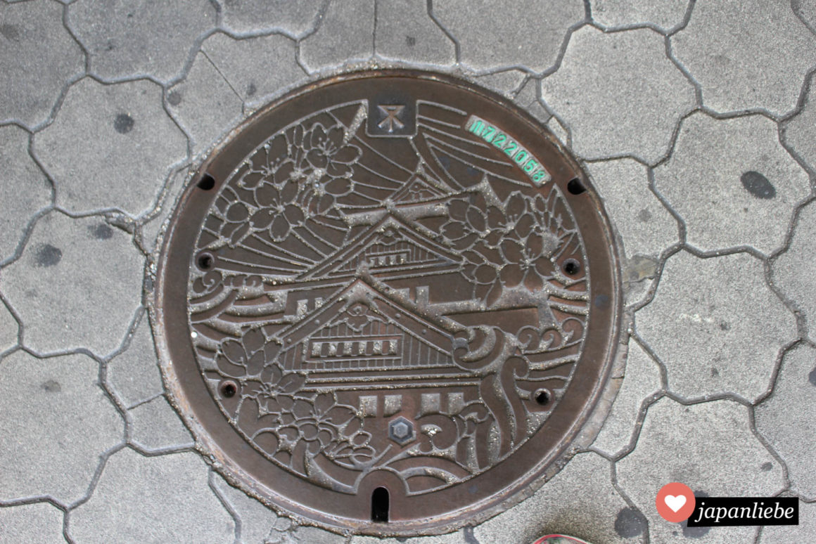 Eine Reihe an Kanaldeckeln in Osaka zeigen die Burg der Stadt mit Kirschblüten.