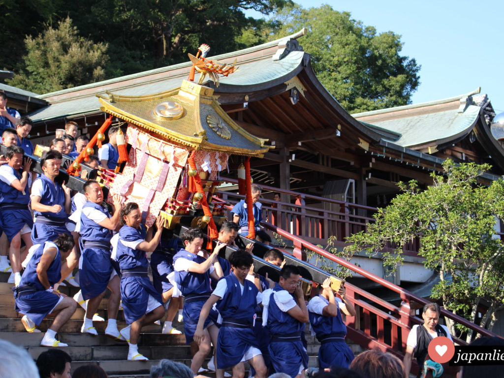 Männer tragen eine schwere o-mikoshi Göttersänfte die Treppe am Suwa Schrein in Nagasaki hinab. Hier ist Teamwork gefragt.