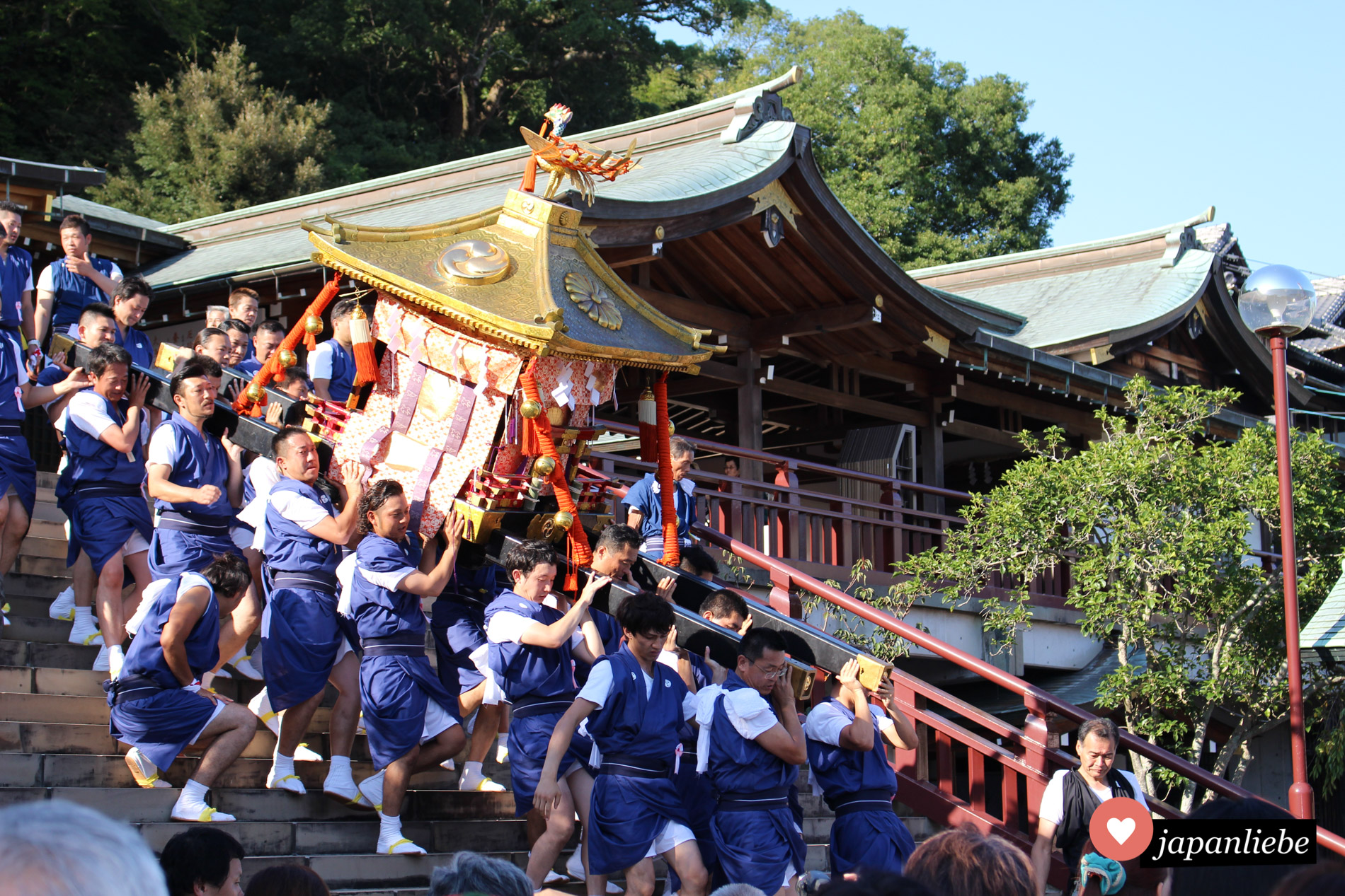 Männer tragen eine schwere o-mikoshi Göttersänfte die Treppe am Suwa Schrein in Nagasaki hinab. Hier ist Teamwork gefragt.