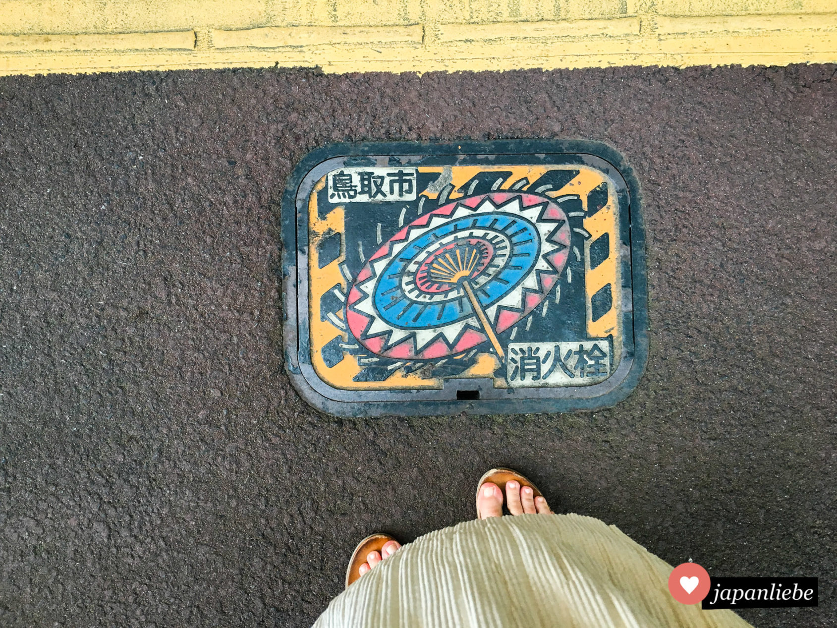 Ein Löschwasser-Kanaldeckel in der japanischen Stadt Tottori zeigt einen bunten Shanshan-Papierschirm.