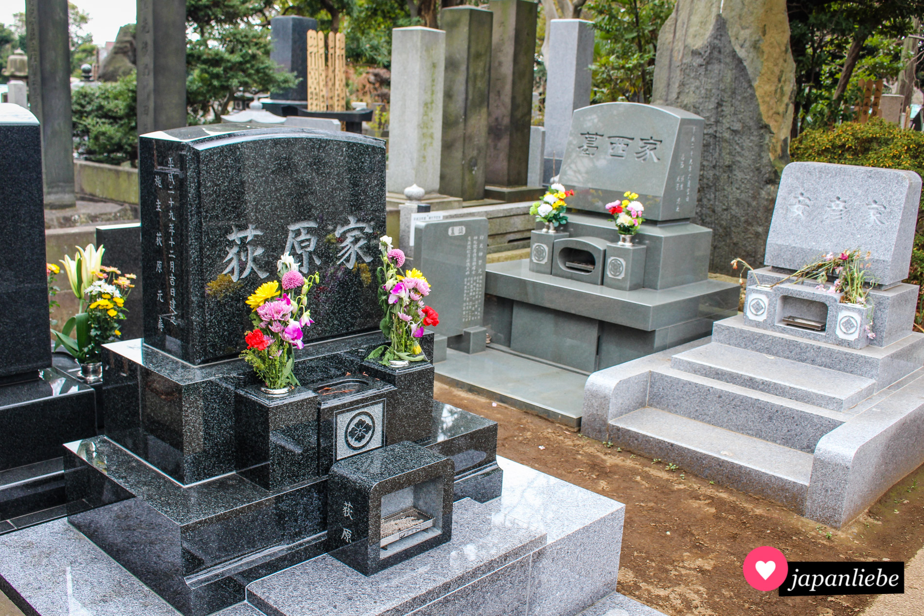 Ein typisch japanisches Grab mit Inschriften an der Seite des Grabsteins, Blumenvasen und einer Möglichkeit, Räucherstäbchen anzubrennen.
