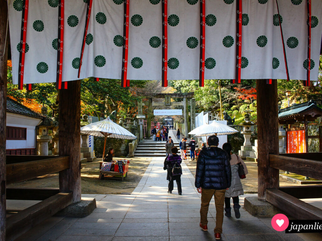 Blick durch das Eingangstor des Kotohira-gū-Schreins auf die „fünf Bauern“ genannten Verkaufsstände für kamiyoame-Bonbons.