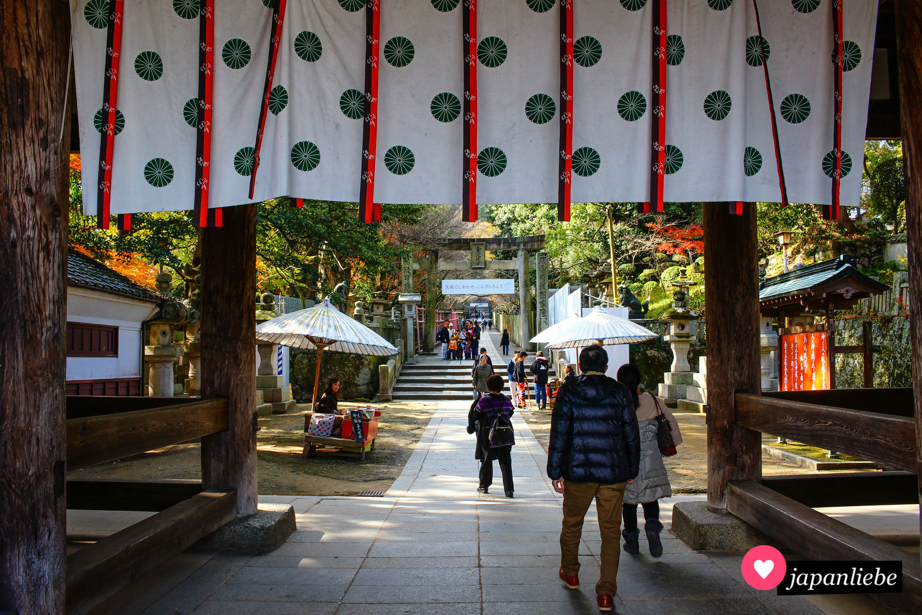 Blick durch das Eingangstor des Kotohira-gū-Schreins auf die „fünf Bauern“ genannten Verkaufsstände für kamiyoame-Bonbons.