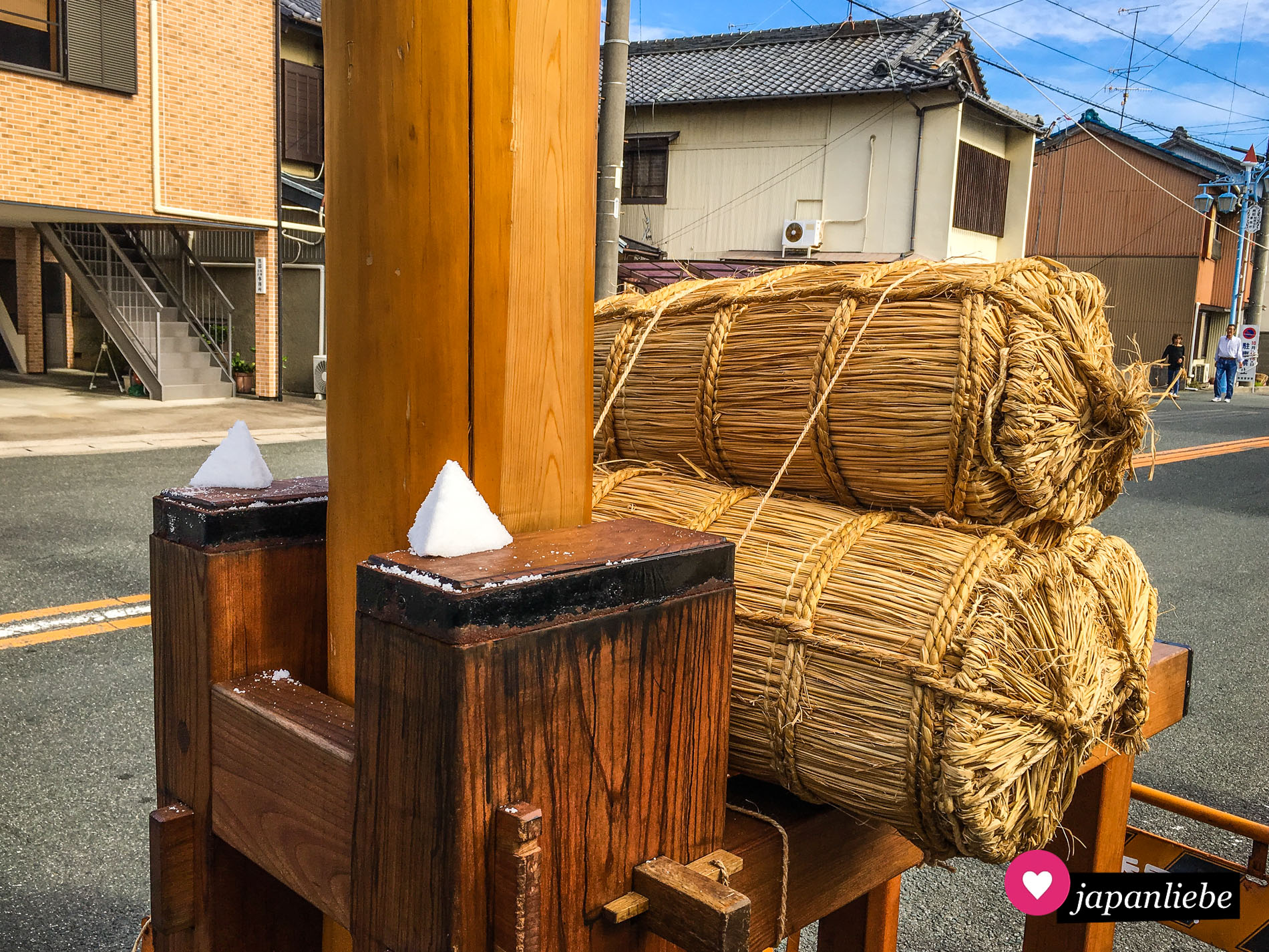 Salzkegel zieren als Schutz den Fahnenmast an einem Schrein in Gamagōri, dessen Gottheit gerade in einer Sänfte durch die Straßen getragen wird.