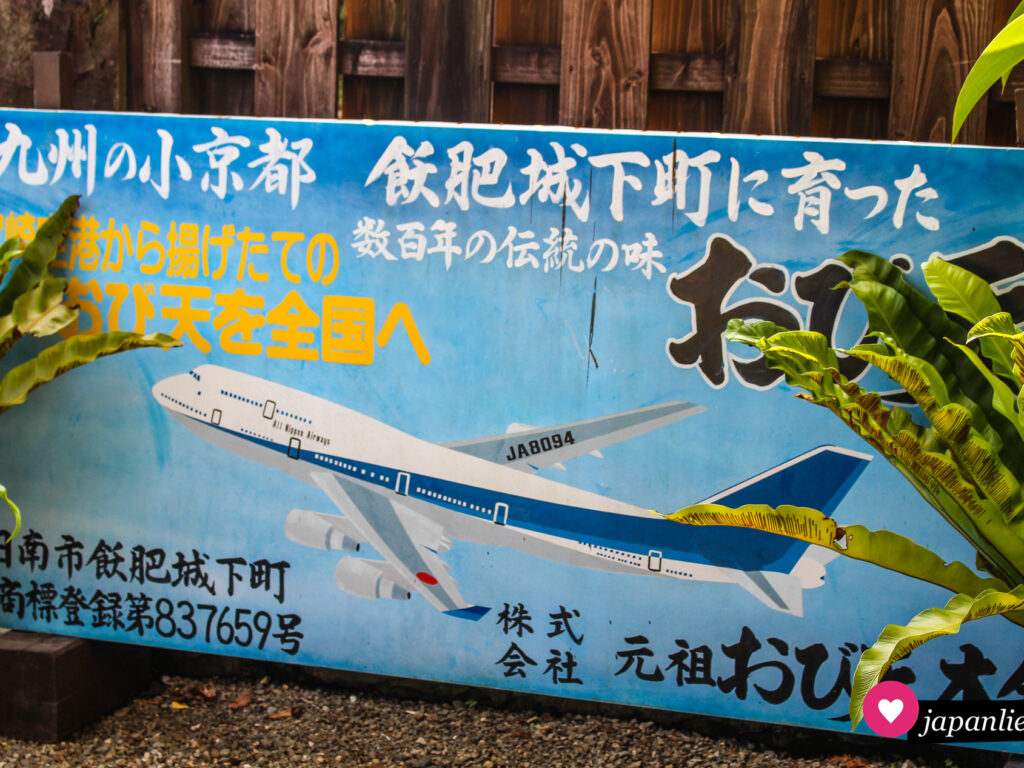 Ein Werbeschild von Air Nippon Airways ruft dazu auf die Stadt Obi, das „kleine Kyōto Kyūshūs“ zu besuchen.
