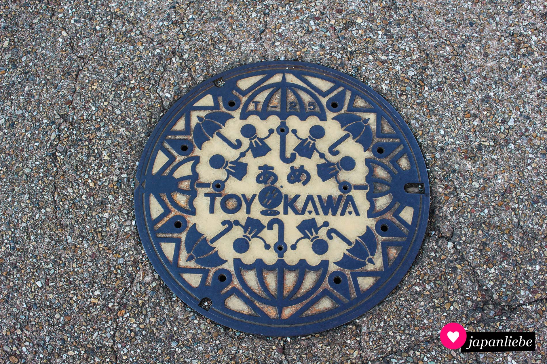 Viele „teru teru bōzu“-Püppchen bilden umringt von Regenschirmen einen Kreis. In der Mitte des Gullydeckels steht auf japanisch das Wort „ame“ für Regen.