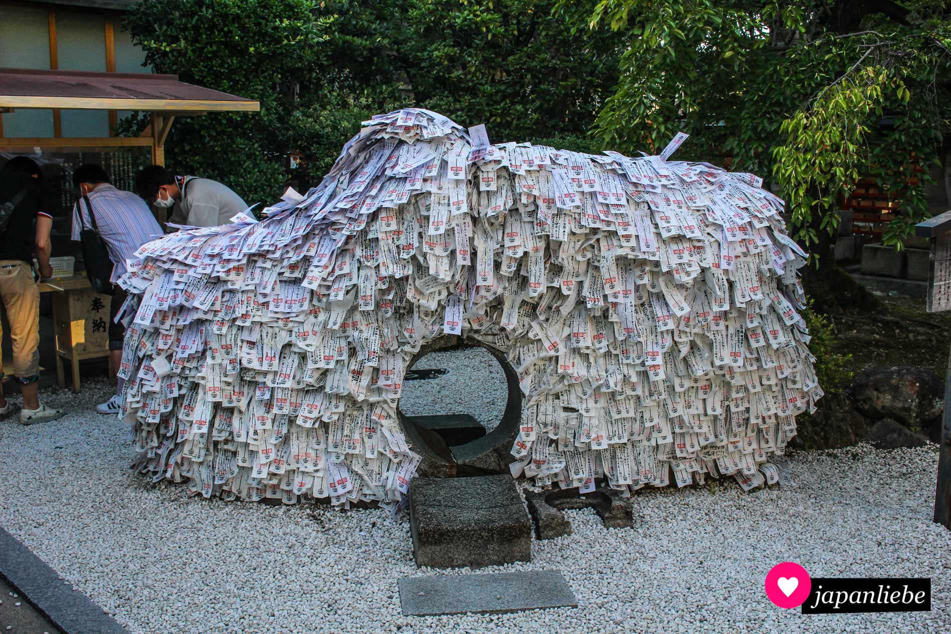 Ein paar junge Männer schreiben ihre Wünsche auf *katashiro*-Papieramulette, um sie nach dem Loslass-Ritual auf den Stein zu kleben.